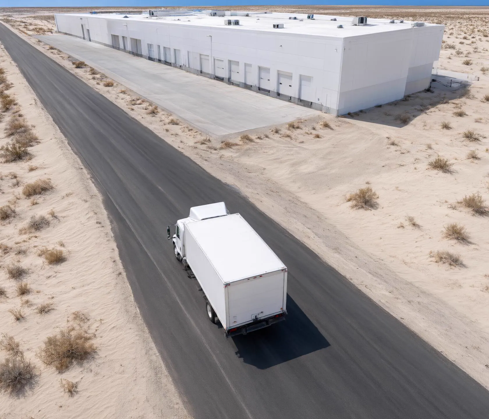 A truck drives along a highway towards a warehouse.